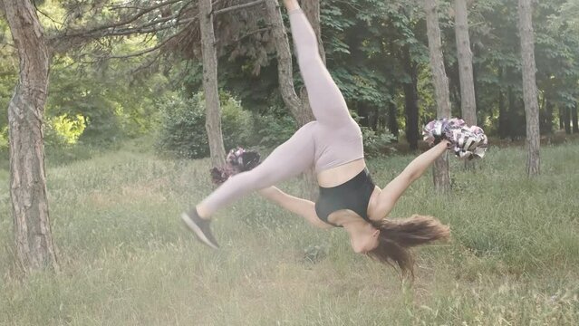 Portrait of beautiful cheerleader woman dancing with pompons outdoors in the park on sunset