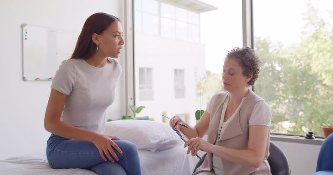 Caucasian woman chiropractor consulting with a young patient in an office. Mixed race woman getting advice about spine adjustment for better posture and alignment at a spa with mature physiotherapist
