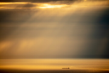 Container ships on the open ocean with dramatic golden light beams forming through clouds at sunset.