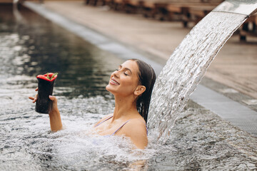 Young beautiful woman in bikini drinking cocktail getting hydrotherapy in outdoor pool