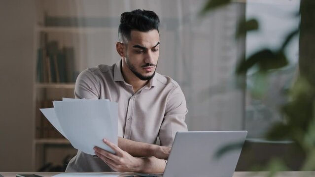 Upset businessman arab guy copy paper text at computer electronic form feel nervous frustrated hispanic man check documents financial report develop statistic plan pay bank debt in online application