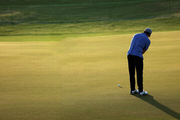 Male golf player wearing white shirt putting on sunny day