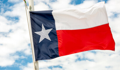 Texas State Flag proudly flying in the partly cloudy blue sky.