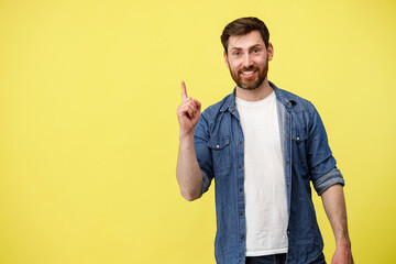 Smiling man raised finger up as sign he has new idea on yellow studio background