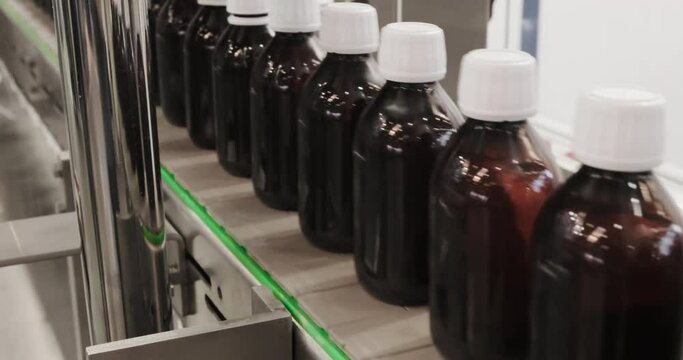 Close-up Many glass bottles for packaging liquid medicines or cosmetics in a row on a conveyor belt in a pharmaceutical manufacturing factory 4K DCI