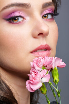 Closeup portrait of female face with pink beauty makeup and carnation flowers near lips.