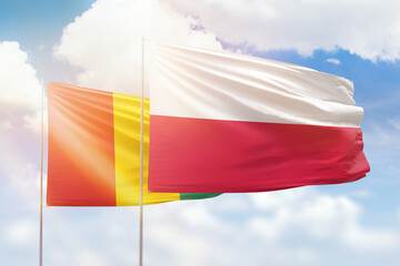 Sunny blue sky and flags of poland and guinea