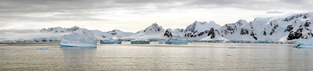 Panorama of icebergs floating in the bay, in front of snow covered moutains at Portal Point in Antarctica