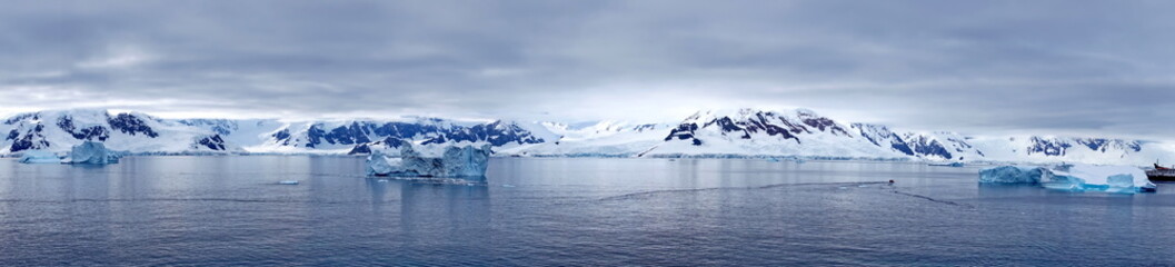 Fototapeta na wymiar Panorama of icebergs floating in the bay, in front of snow covered moutains at Portal Point in Antarctica