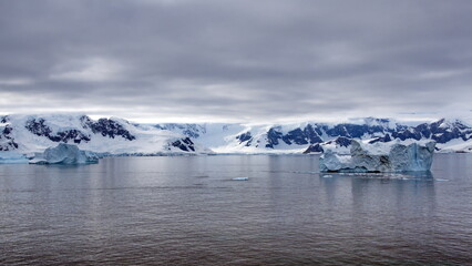 Fototapeta na wymiar Icebergs floating in the bay in front of snow covered mountains at Portal Point in Antarctica