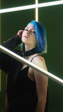 Futuristic model. Cyberpunk fashion. Nightclub lifestyle. Pretty confident stylish woman posing leather outfit in LED lamp light on dark studio background vertical.