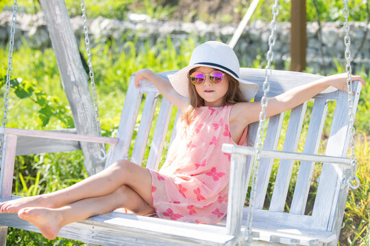 Child playing on swing. Healthy summer activity for children in warm weather. Little kids swinging. Fashion child in summer straw hat and sunglasses.