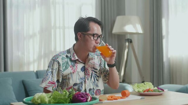 Asian Man Enjoys Drinking Orange Juice While Preparing Healthy Food At Home
