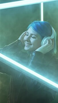 Music chill. Playlist joy. Futuristic gadget. Satisfied relaxed dancing woman in headphones listening to song in LED lamp light on dark smoke background.