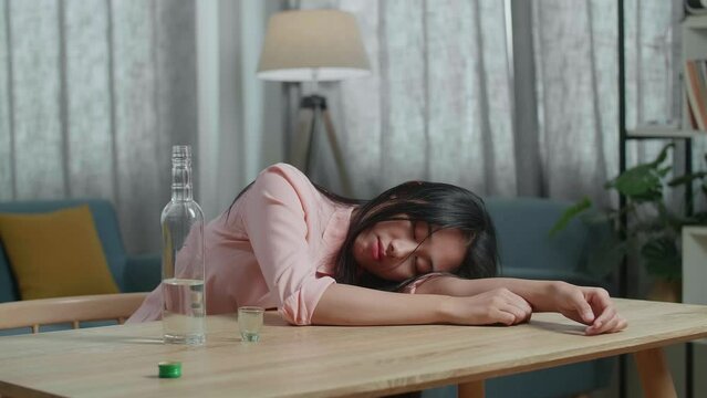 Drunk, Depressed Asian Woman Drinking Vodka Before Using A Fist Smashing The Table At Home

