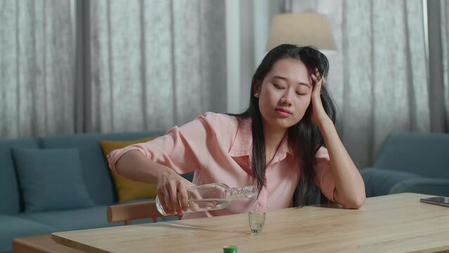 Drunk, Depressed Asian Woman With Smartphone On Table Drinking Vodca From The Bottle At Home
