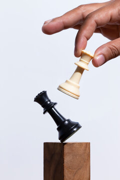 Hand Holding Chess Queen Figure And Knocking Down The Queen. Business Concept.