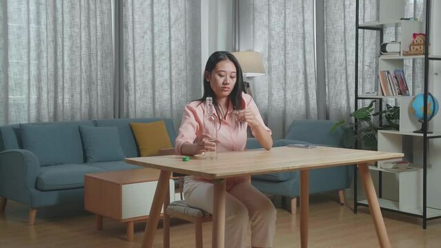 Drunk, Depressed Asian Woman Pouring Vodka In A Shot Glass Before Drinking And Crying At The Home
