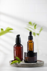 Three different brown glass bottles with eco-friendly organic cosmetic products and green plants in laboratory flasks.