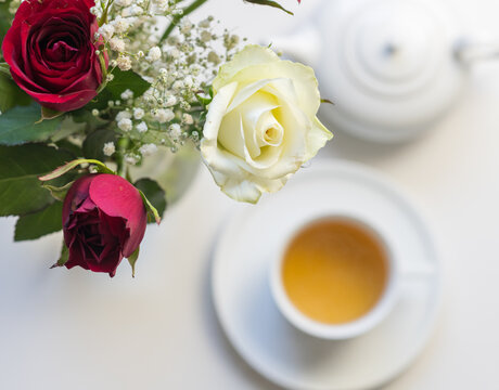 High angle closeup of white and red roses with tea cup and teapot in background (selective focus)