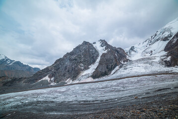 Dramatic landscape with glacier tongue and icefall on large snow mountain range with sharp rocky...