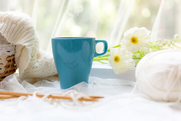 Coffee morning.  Blue steaming cup of hot coffee for relax after working hobbies crochet on white wooden near window with flowers.  .