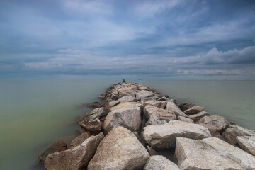 One guy sits on a rock by the sea
