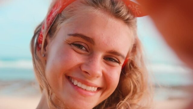 Young cheerful Caucasian woman student shows gesture of heart makes it with hands with smile looks at camera demonstrating love and friendliness stands on beach by ocean. Volunteering, good deeds