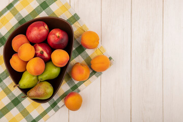 top view of fruits as apricot peach pear in bowl on plaid cloth and on wooden background with copy space