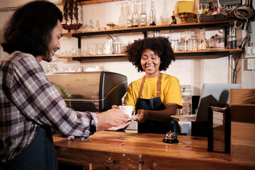 Two cafe business startup partners and friends, African American female, and Thai male baristas work and cheerful smile together at counter bar of coffee shop, happy service job, and SME entrepreneur.