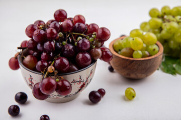 side view of red grape and white grape berries in bowls with grape berries white grape and leaves...