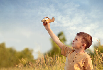 a boy in a yellow T-shirt raised his hand up to the sky and holds a wooden plane in his hand