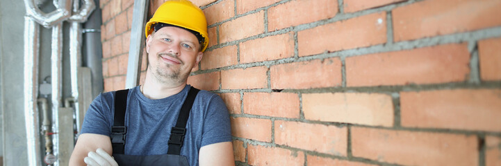 A man in a helmet stands against a brick wall indoors