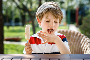 Little preschool boy eating ice cream in summer. Happy child with cold dessert. White chocolate...