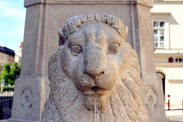 carved stone lion head sculpture, water fountain in public park. steel pipe spout and clear water...