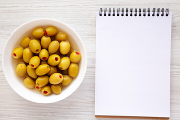Marinated Green Olives with Pimento Peppers in a Bowl, blank notepad, top view. Flat lay, overhead, from above.