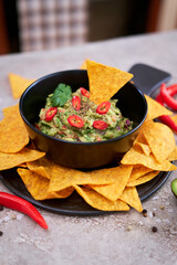 Guacamole dip with tortilla chips or nachos on black serving board