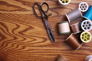 Multicolored threads and old scissors scattered on a wooden table, retro scissors, flat lay, copy space.