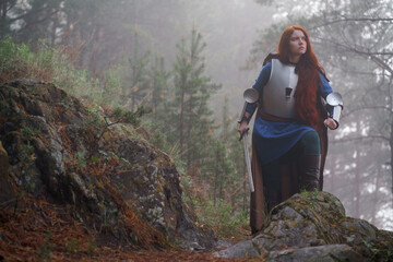 Young red-haired girl in medieval knight's armor in summer forest