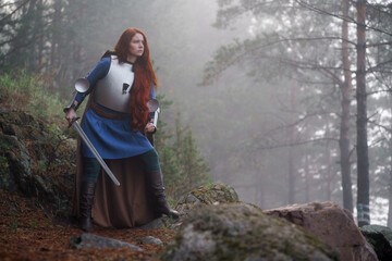 Naklejka premium Young red-haired girl in medieval knight's armor in summer forest
