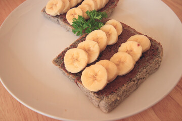 Whole grain bread loaf with chocolate spread topped with banana slices for a healthy vegan breakfast and a healthy sustainable lifestyle