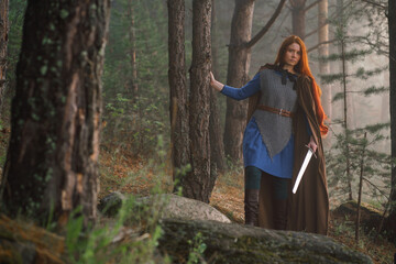 Red-haired girl in armor and raincoat in forest. Historical concept