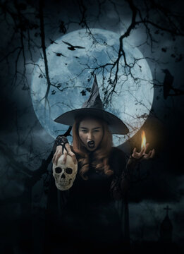 Halloween witch holding a skull standing over cross, church, crow, birds, dead tree, full moon and cloudy spooky sky, Halloween mystery concept