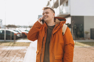 Casual Young blonde man with backpack talking on mobile phone in the city. Portrait of happy man talking with friend on phone. Phone Communication. Urban lifestyle concept. Traveler