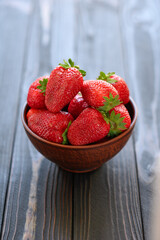 A bowl of red juicy strawberries on rustic wooden table. Healthy and diet snack food concept.