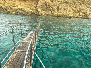 yacht in the open sea. sea with a sandy beach against the backdrop of a mountain. on the yacht a wooden bridge with metal handrails for tourists jumping into the water from a height