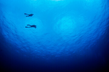 Blue ocean background with a lot of copy space and a silhouette of a couple of divers