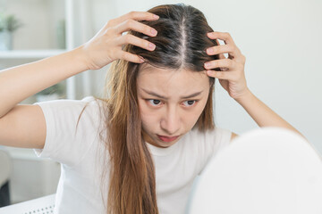 Naklejka premium Damaged Hair, face serious asian young woman worry looking at scalp in mirror, hand in break into front hair loss, thin problem symptom at home. Health care shampoo beauty, isolated on background.