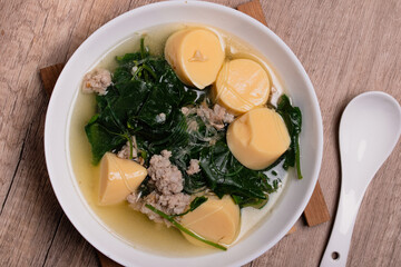 Vegetable gourd soup with minced pork and egg tofu in white bowl on wooden background Thai food.(gaeng jued tum luang)