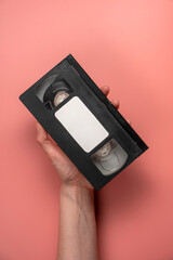 Woman's hand holding old video tape on pink background. VHS video tape.